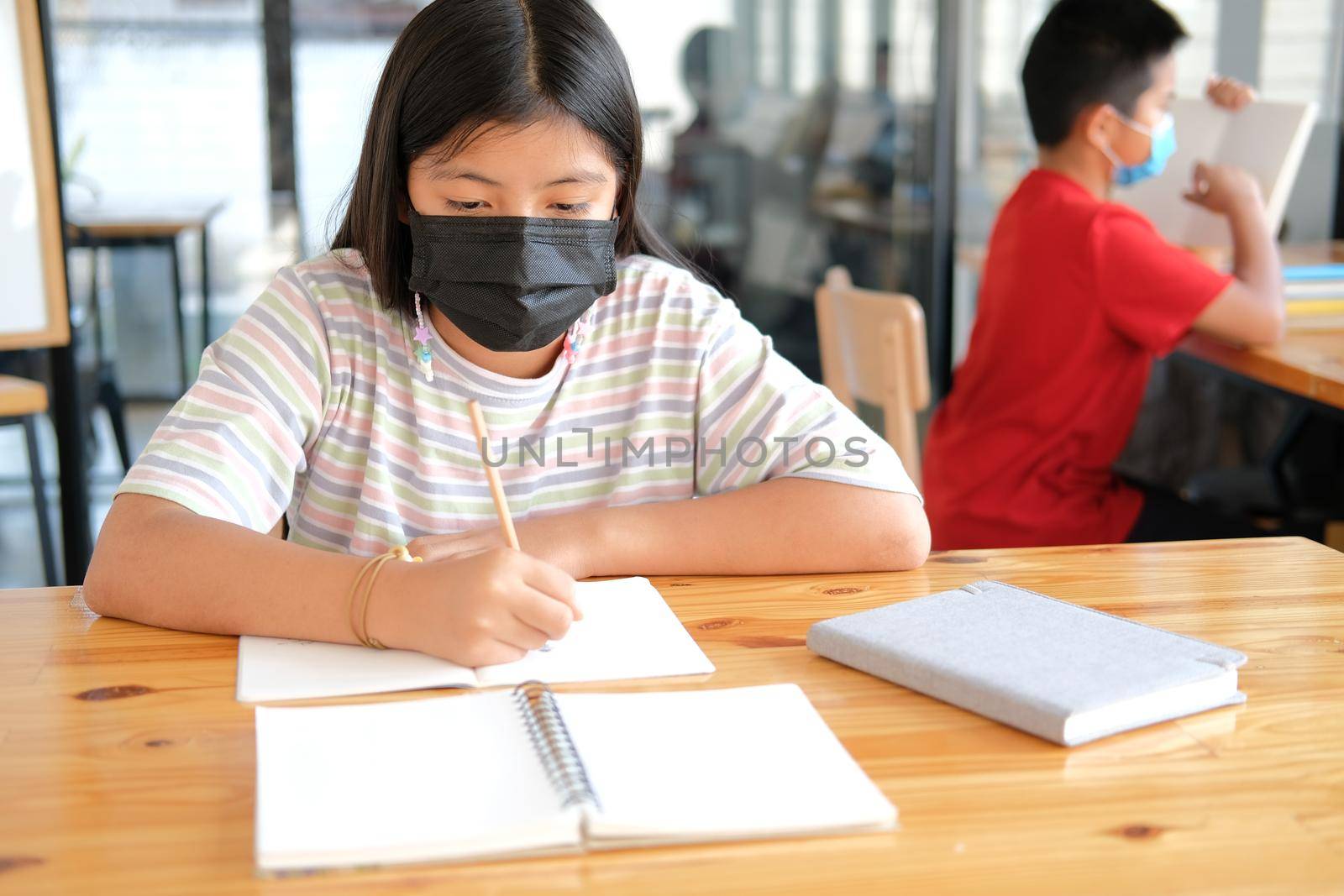 asian girl student wearing face mask studying writing notes doing homework in library. learning education at school