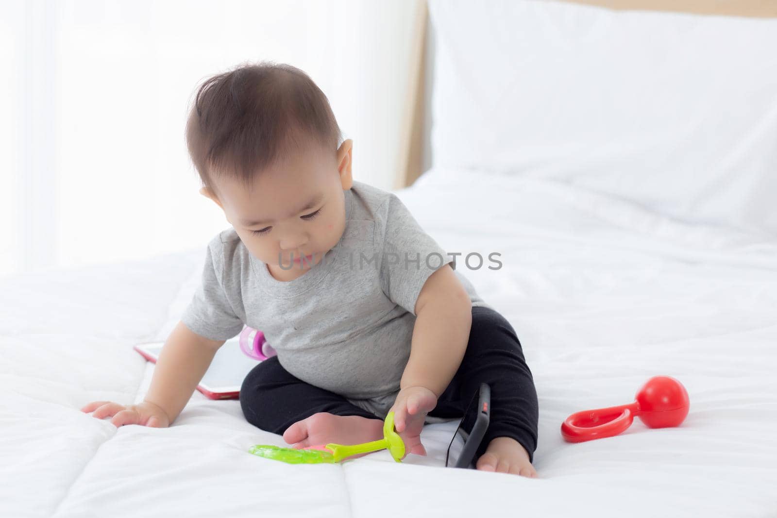 Portrait of cute little baby girl sitting with cozy on bed at bedroom, happiness of toddler, newborn 6-11 months with innocence and expression with cheerful, child charm, indoors, one person.