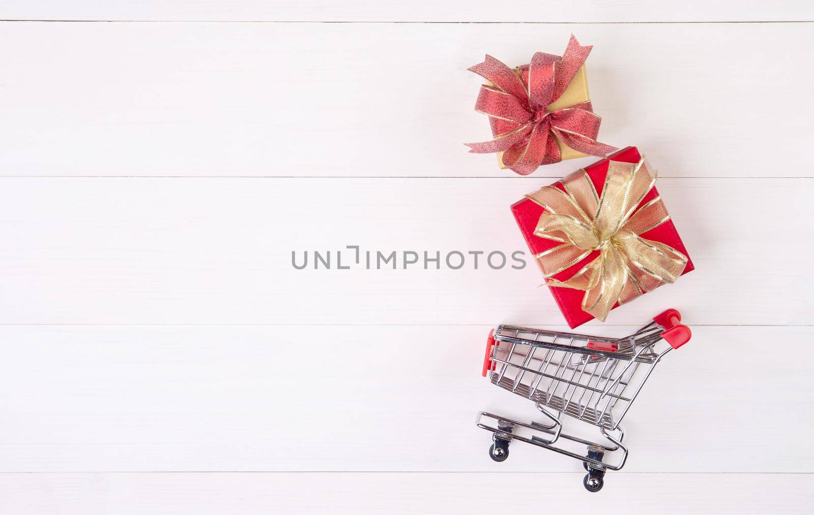 Cart of supermarket and gift box on wooden table, shopping online for presents in valentine day, trolley for sale commerce in holiday and vacation, copy space, celebration and anniversary concept.