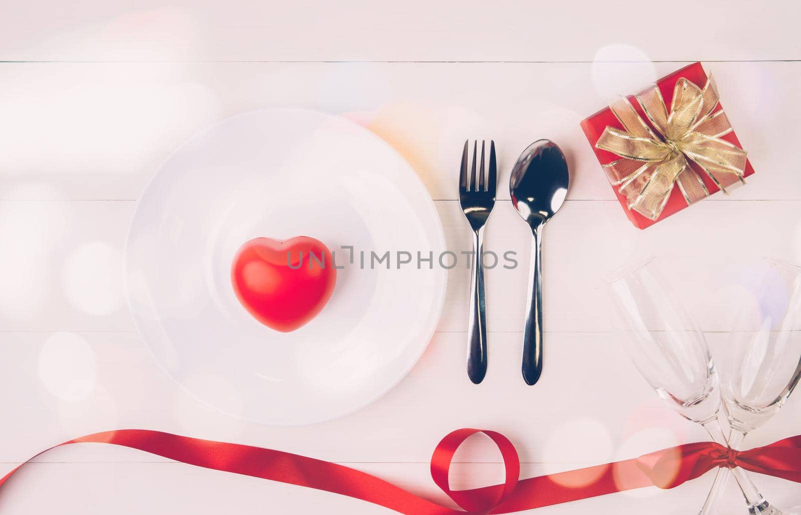 Valentine day concept, wineglass and red ribbon and utensil put in heart on white wooden table background with bokeh, champaign glass on wood desk, couples wine glass together, holiday concept. by nnudoo