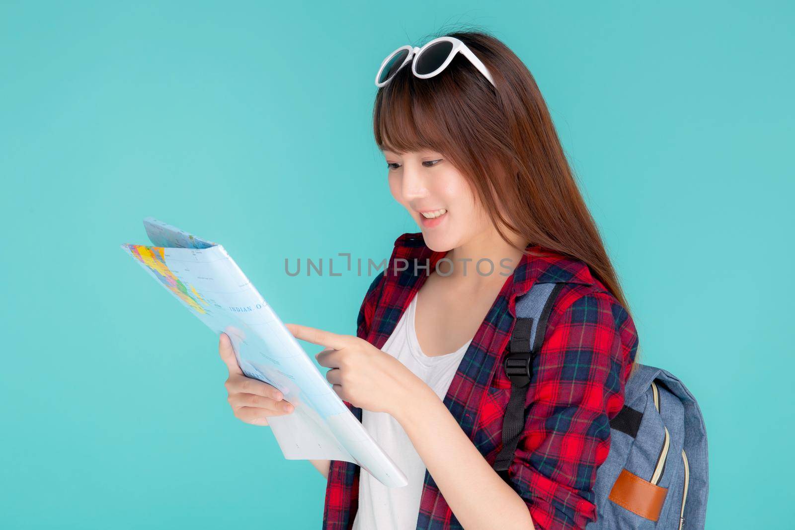 Beautiful happy young asian woman travel looking and pointing a paper map isolated on blue background, asia girl search journey with direction in vacation trip with cheerful for leisure.