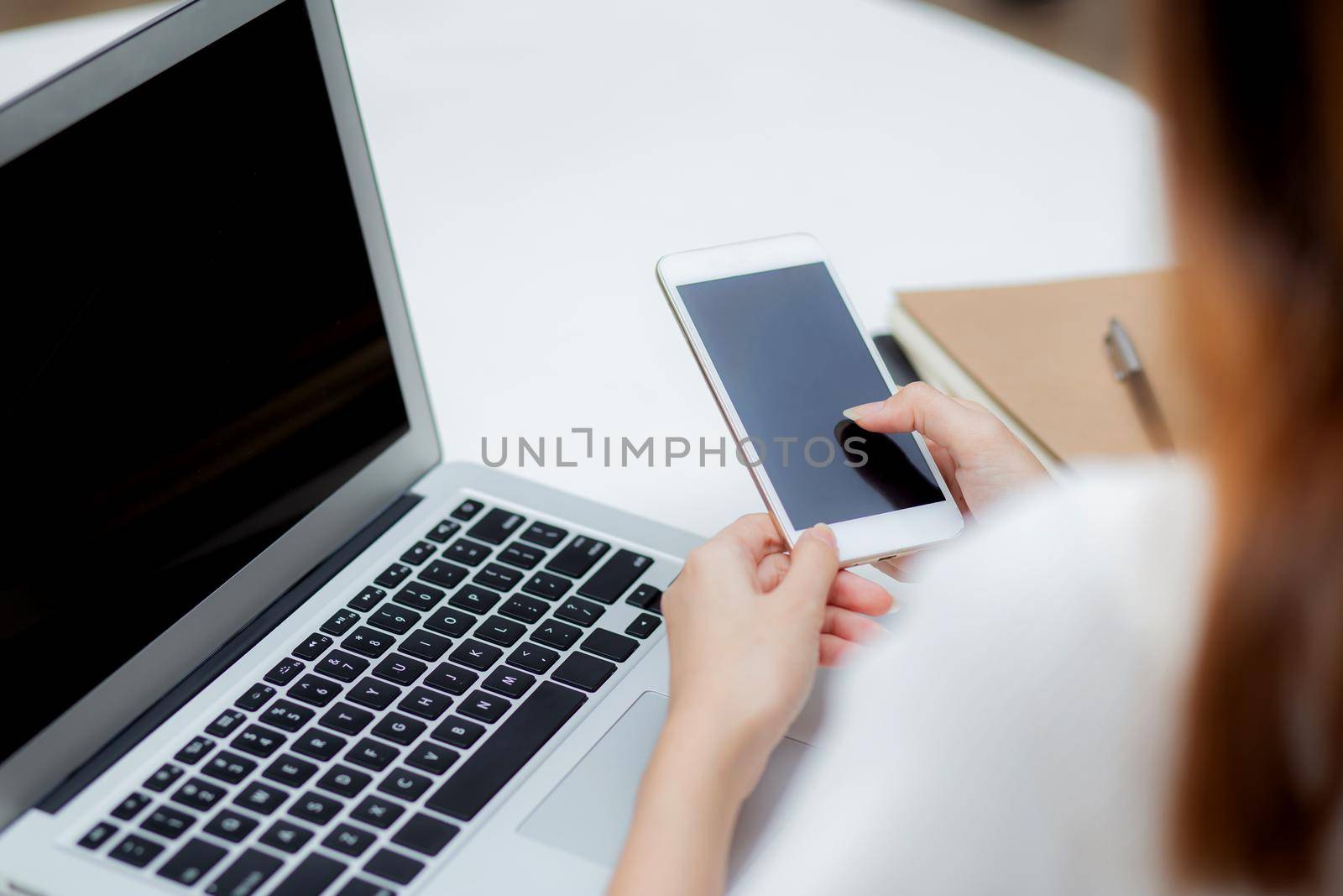 Hand of young woman working with laptop computer and smartphone mockup on desk at home, notebook and phone display blank screen, freelance look message to internet, business and communication concept.