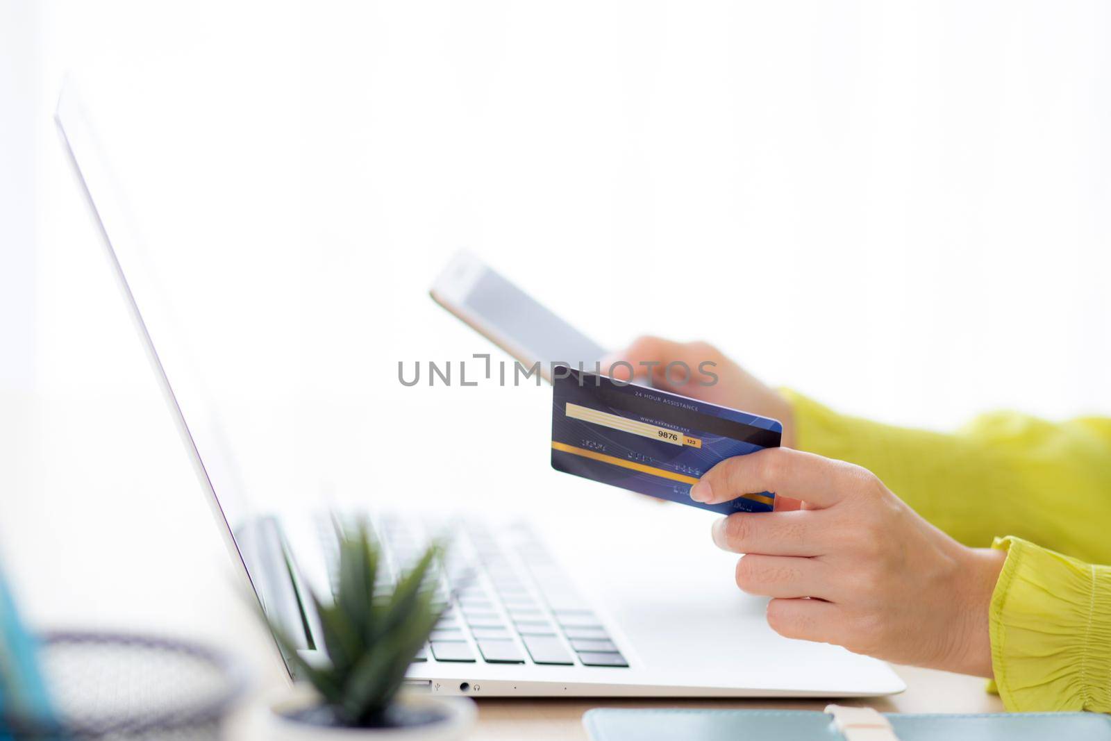 Closeup young asian business woman using smart phone and holding credit card while online shopping and payment with laptop computer on desk at home, female holding debit card, communication concept.