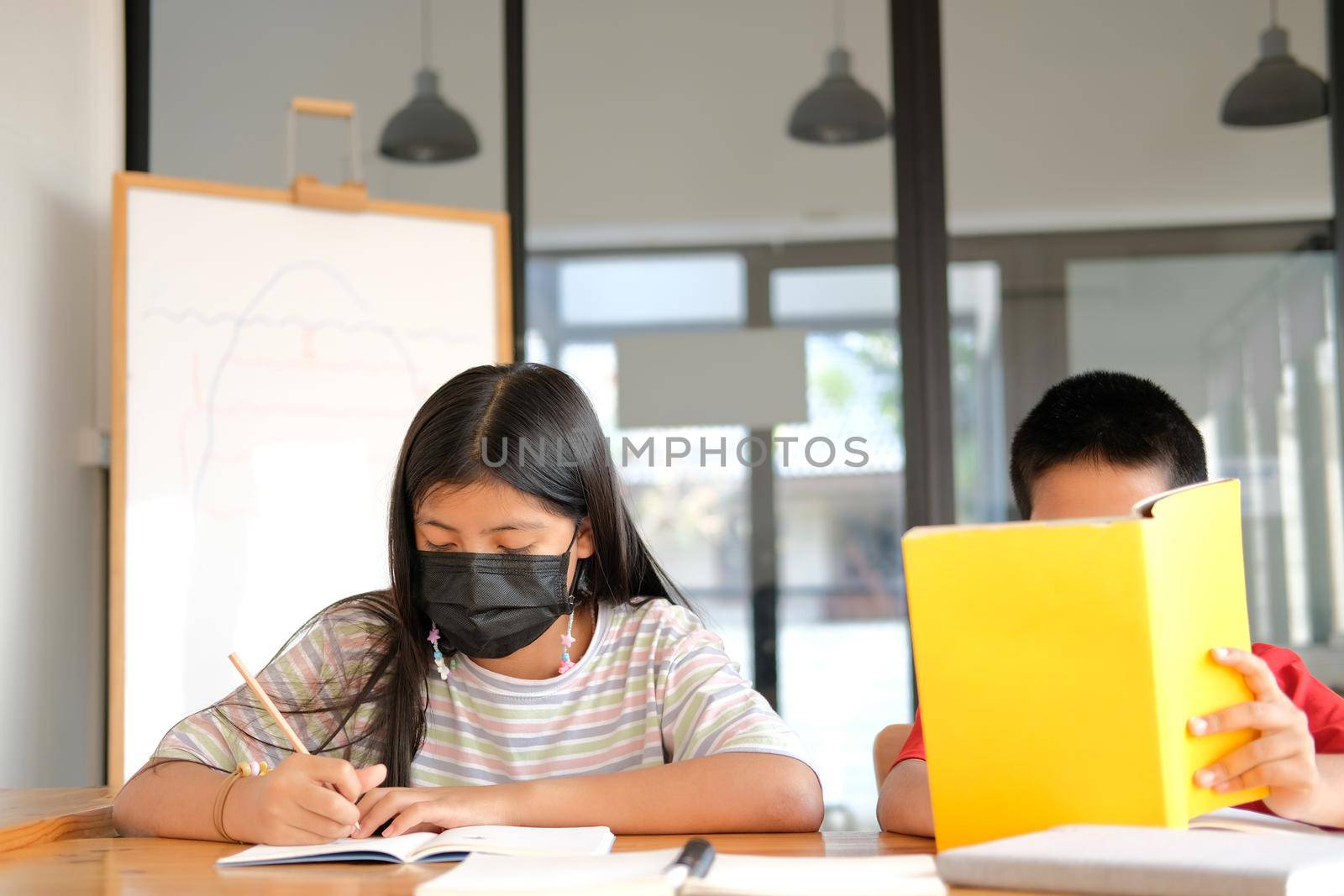 asian girl boy student wearing face mask studying writing notes doing homework in library. learning education at school