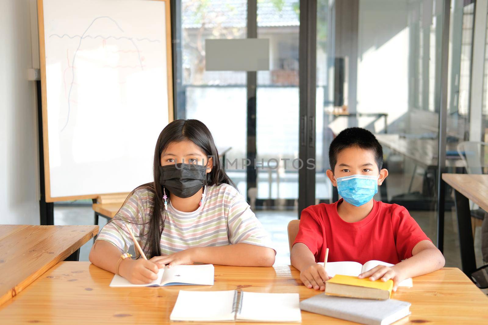 asian girl boy student wearing face mask studying writing notes doing homework in library. learning education at school