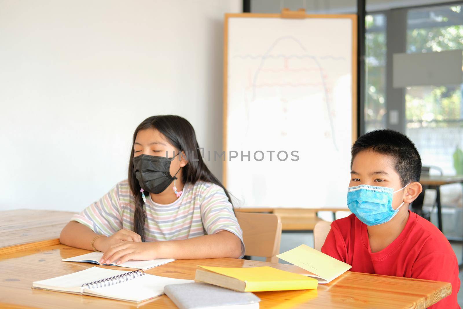 asian girl boy student wearing face mask studying writing notes doing homework in library. learning education at school