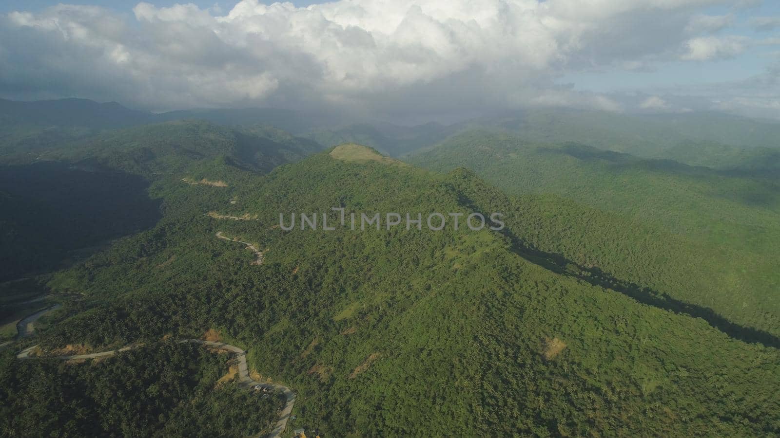 Aerial view of mountains covered rain forest, trees with clouds and sky. Luzon, Philippines. Slopes of mountains with evergreen vegetation. Mountainous tropical landscape. Cordillera region.