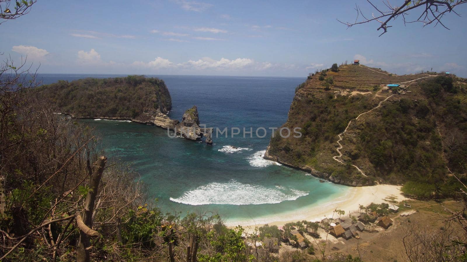 Beach with with azure water, rocky mountains and clear water at sunny day. Clear blue ocean waves rolling to the beach. Nusa Penida, Bali, Indonesia. Travel concept.