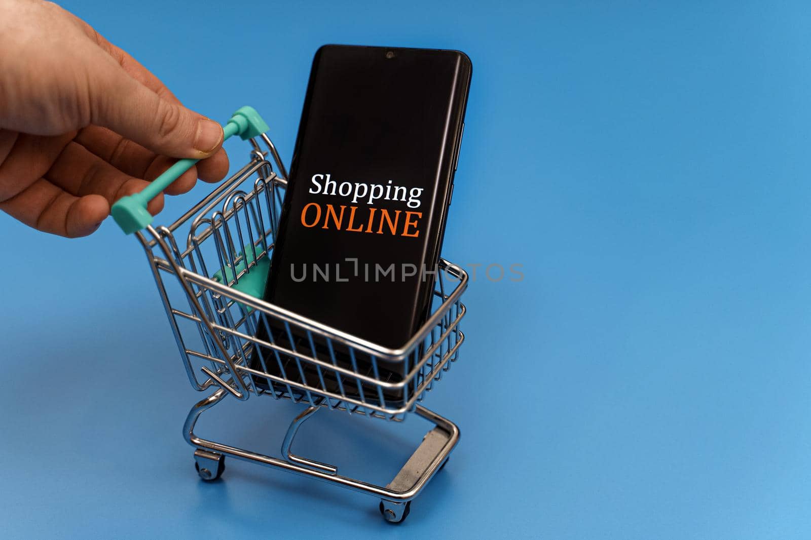 Shopping cart with smartphone on blue background. Online shopping concept.