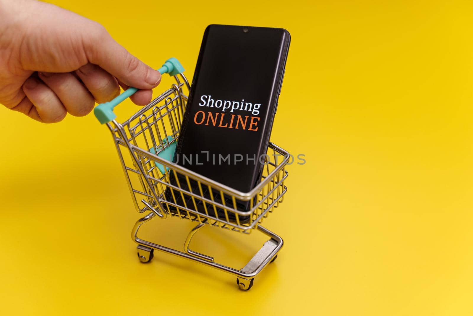 Shopping cart with smartphone on yellow background. Online shopping concept.