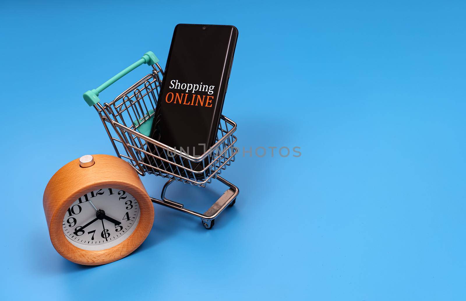 Shopping cart with smartphone and clock. Online shopping concept.