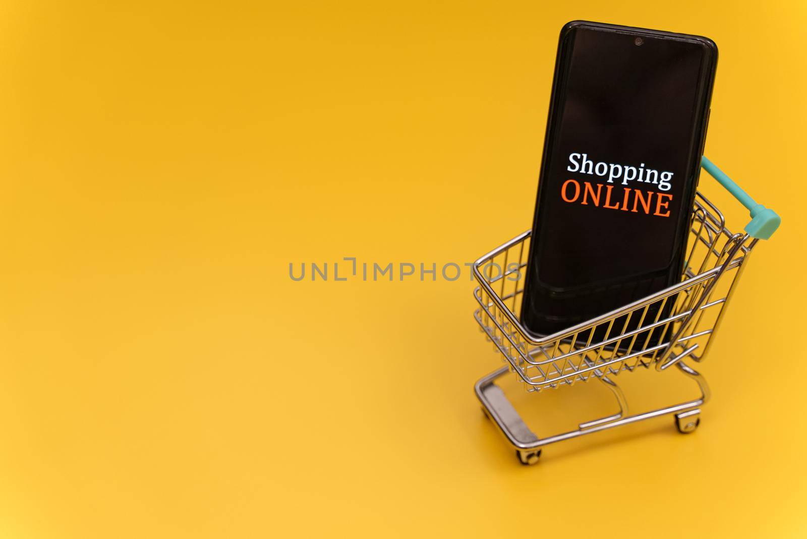 Shopping cart with smartphone on yellow background. Online shopping concept. by dmitrimaruta