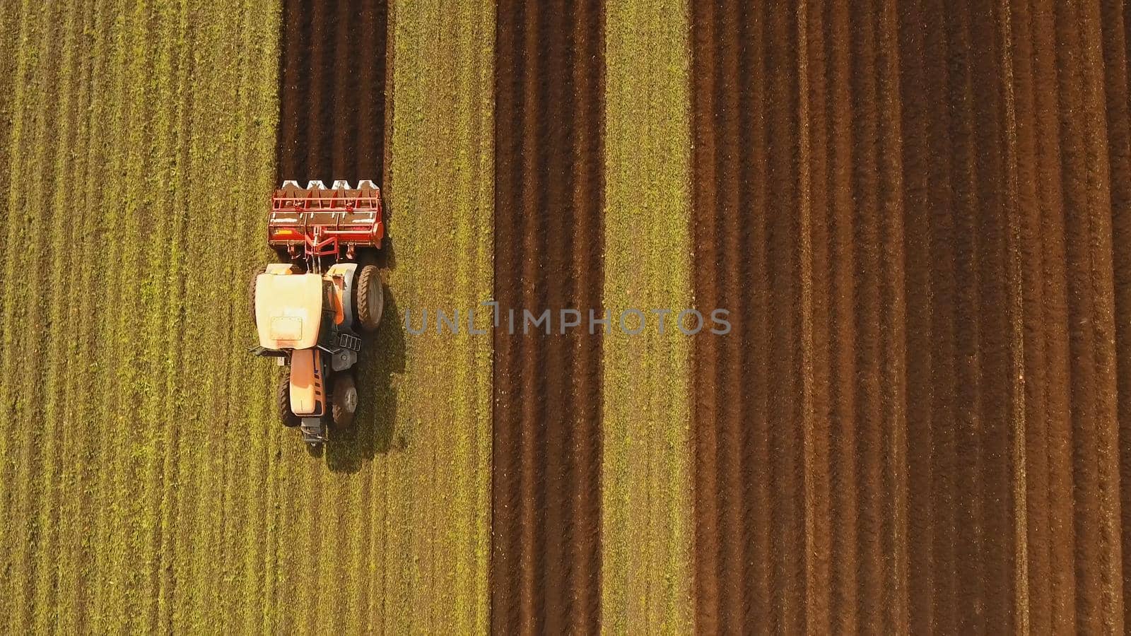 Farmer in tractor preparing land with seedbed cultivator in farmlands. Tractor plows a field. Agricultural work in processing, cultivation of land. Farmers preparing land and fertilizing. Agricultural workers with tractors.