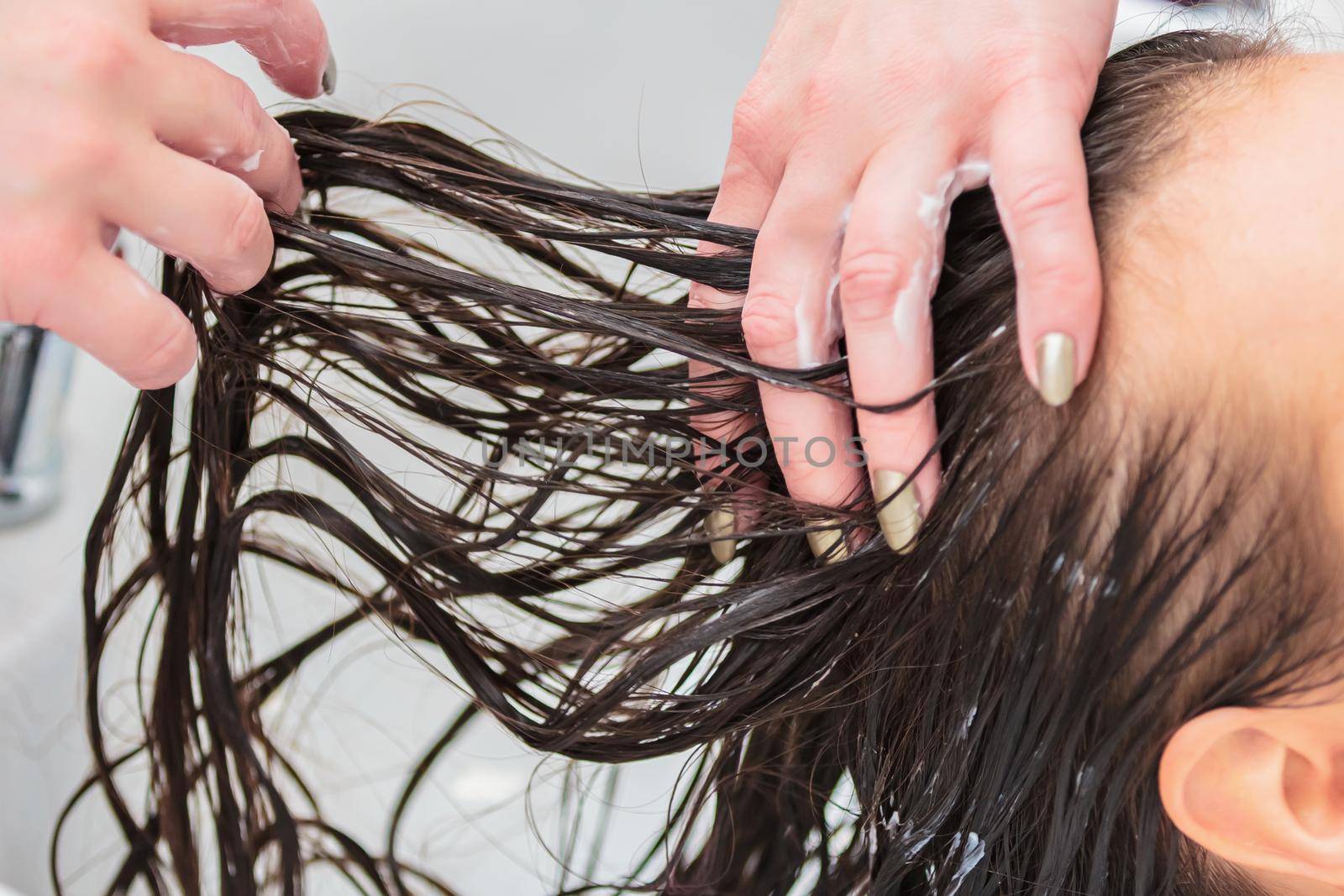 The hairdresser washes the head of a girl with long hair in the sink. Brown hair, close up