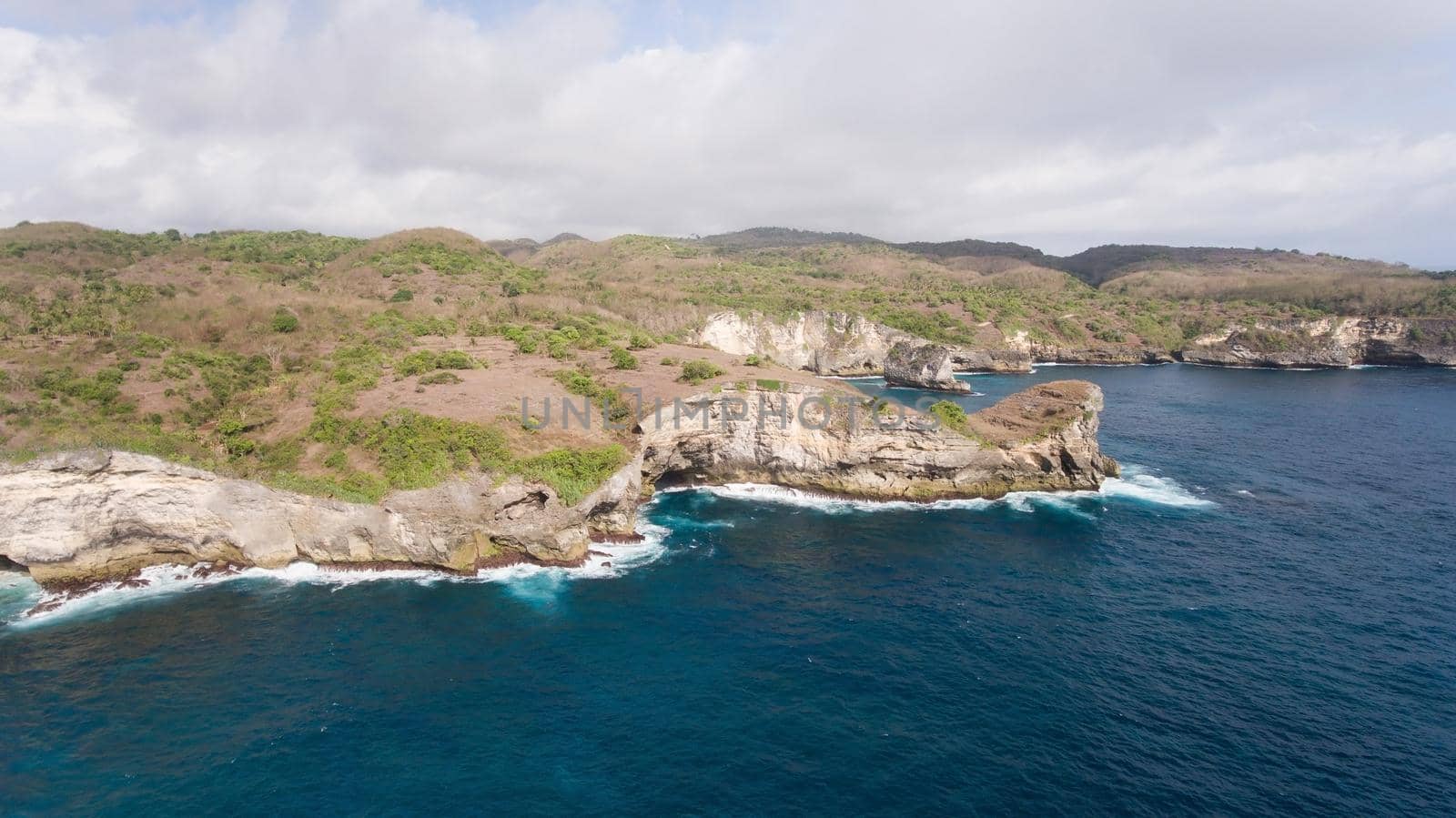 Rocky coast with high cliffs, sea surf with breaking waves on the coast, Nusa Penida, Indonesia. Ocean with waves and rocky cliff. Travel concept.