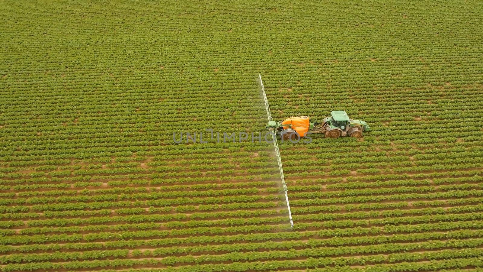 Aerial view tractor spraying the chemicals on the large green field. Spraying the herbicides on the farm land. Treatment of crops against weeds.