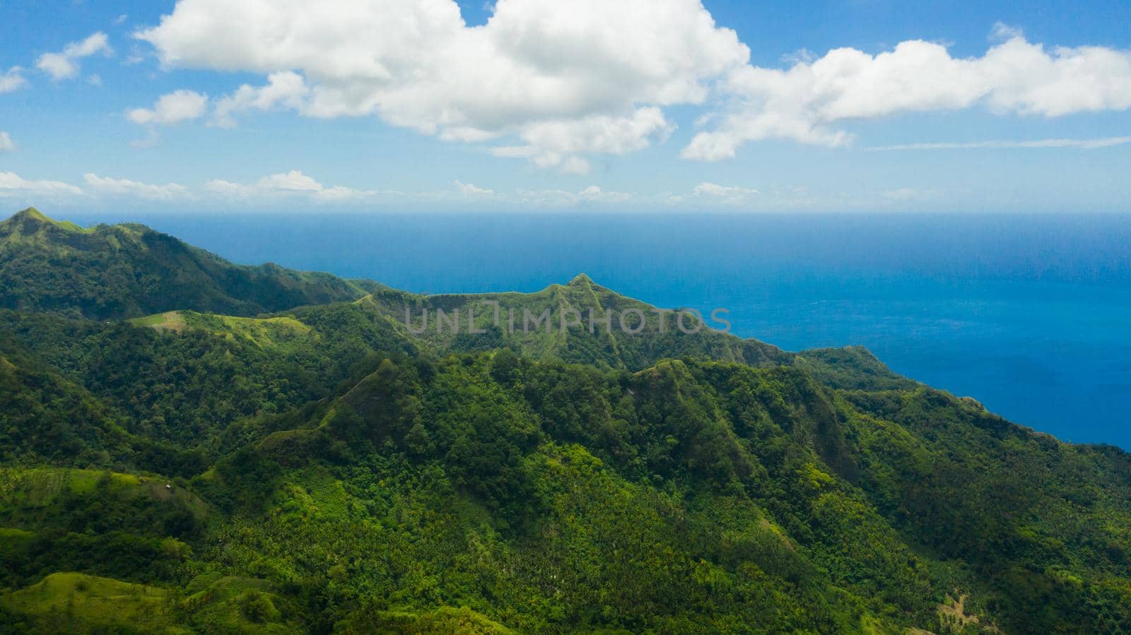 Mountain landscape on tropical island with with blue sea, mountain peaks covered with forest. Slopes of mountains with evergreen vegetation. Philippines, Mindanao