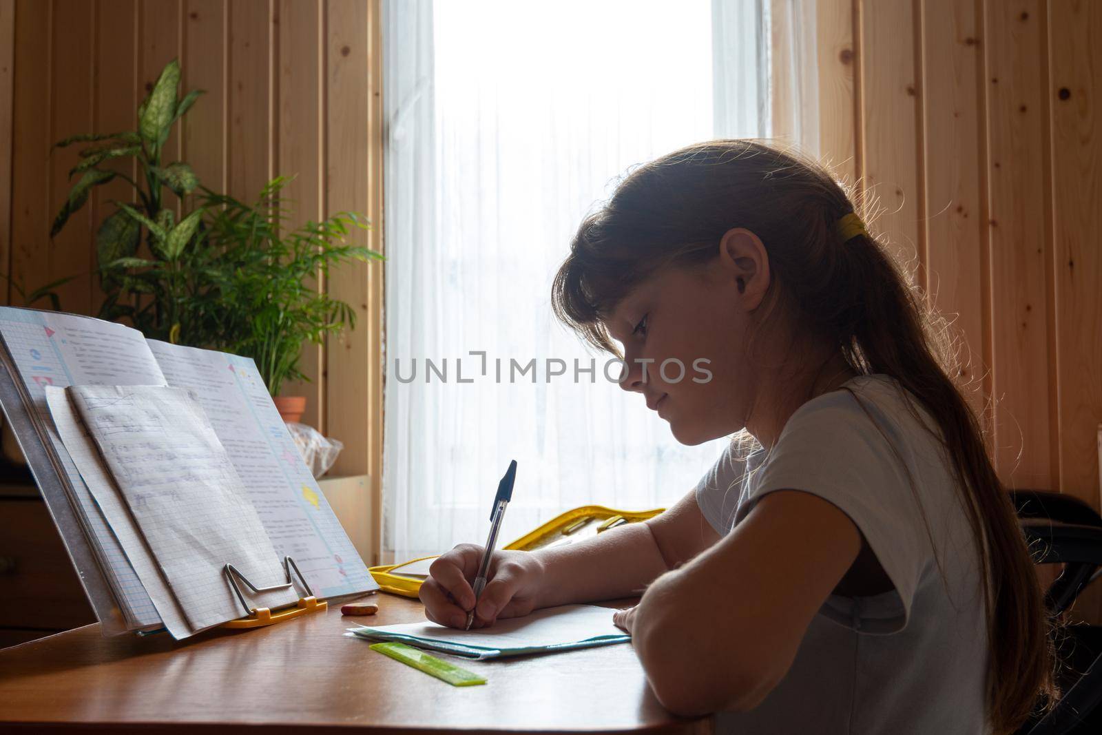 Girl does homework while sitting at the table in the room of a country house