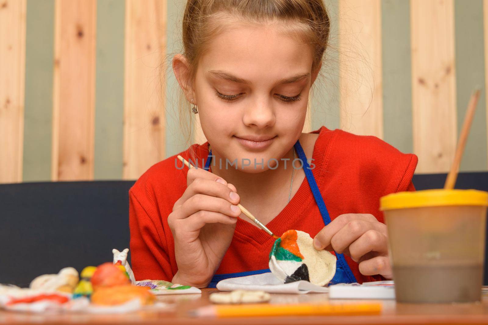 A girl paints a craft from salt dough with watercolors