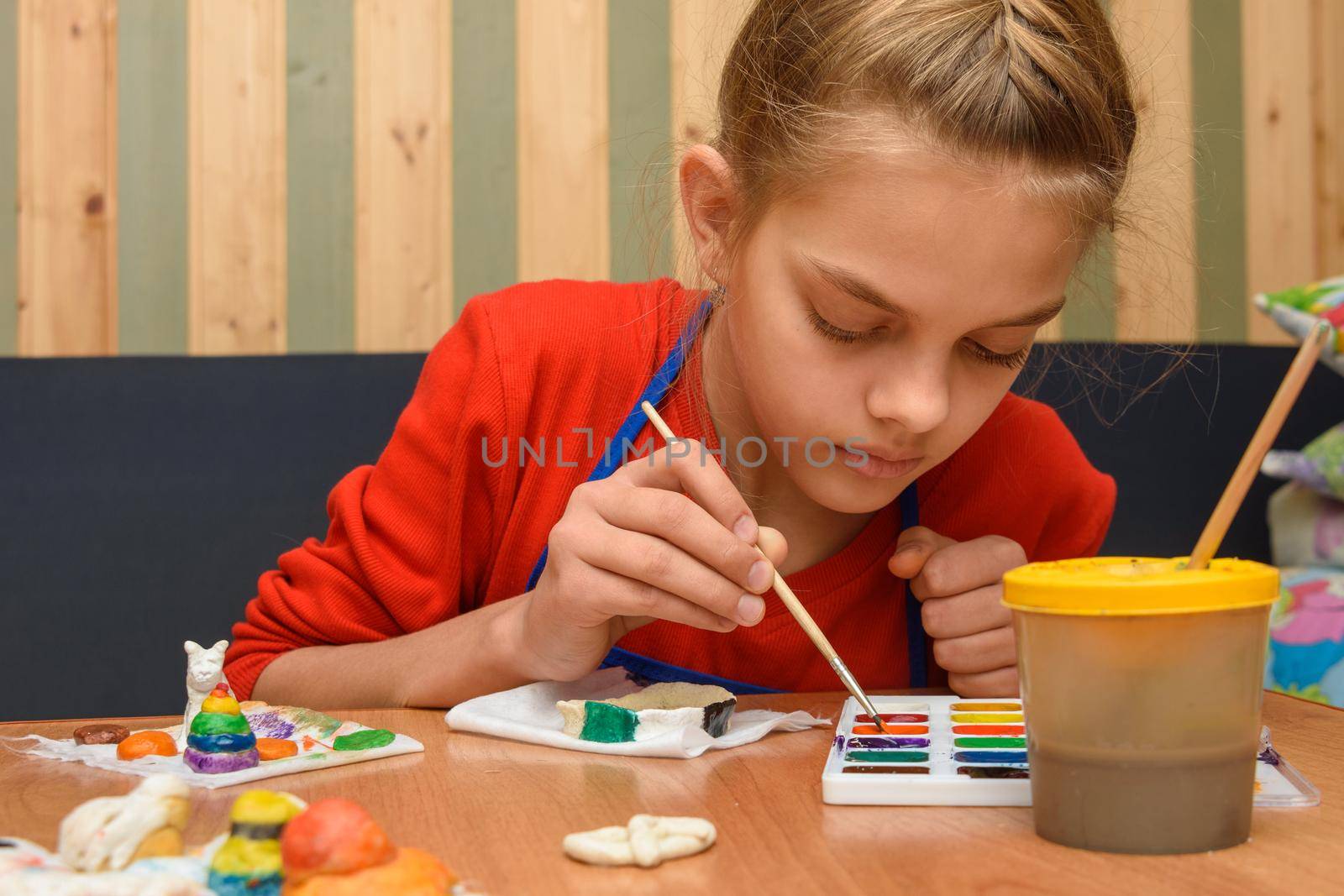 A girl dips a brush in paint of the desired color while painting a craft from salt dough