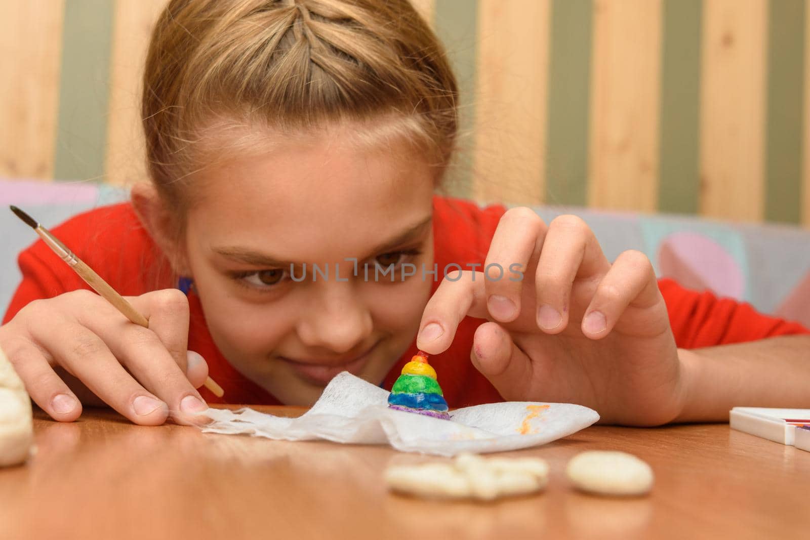 A girl bending over looks at a painted figurine made of salt dough