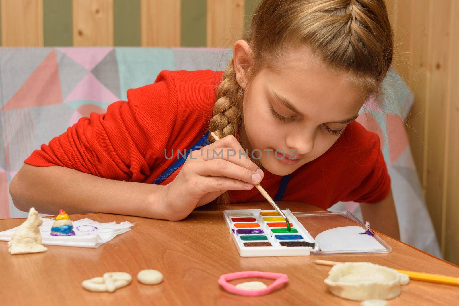 A girl chooses a color of watercolors for coloring dough figurines