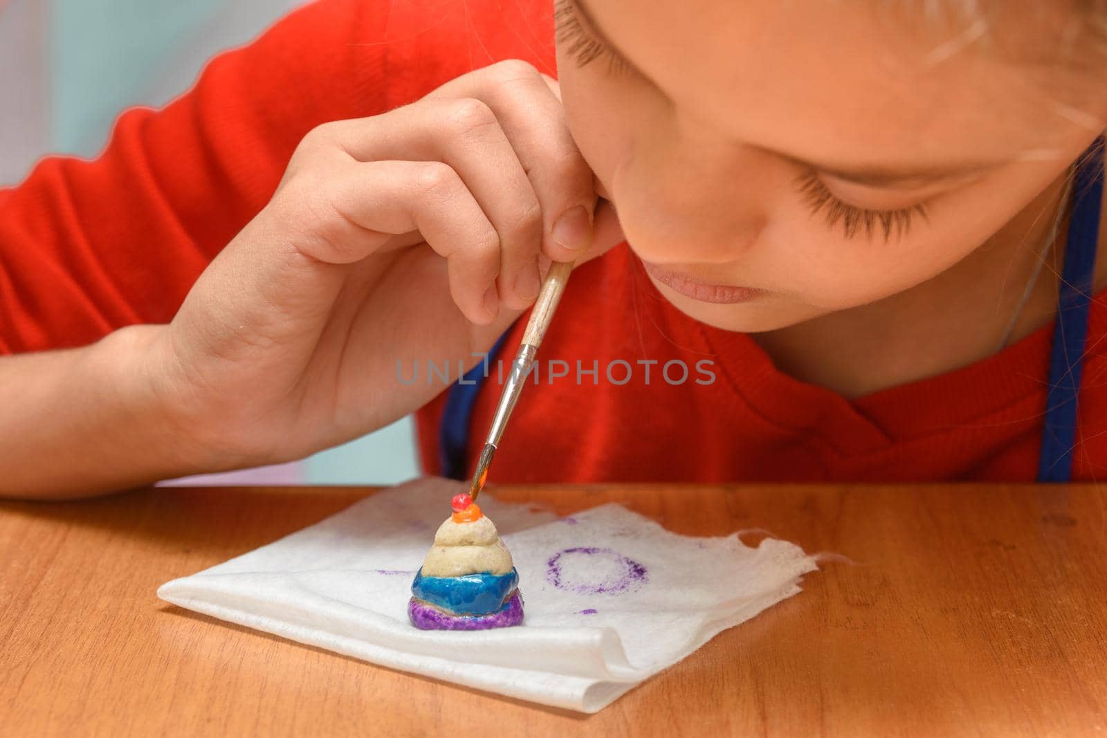 A girl carefully paints a figurine made of salt dough, close-up