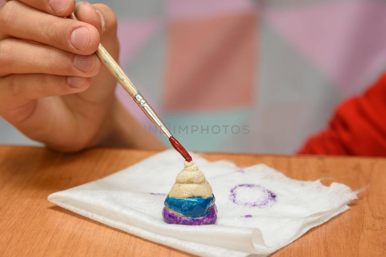 A girl paints a pyramid of salt dough with different colors, close-up