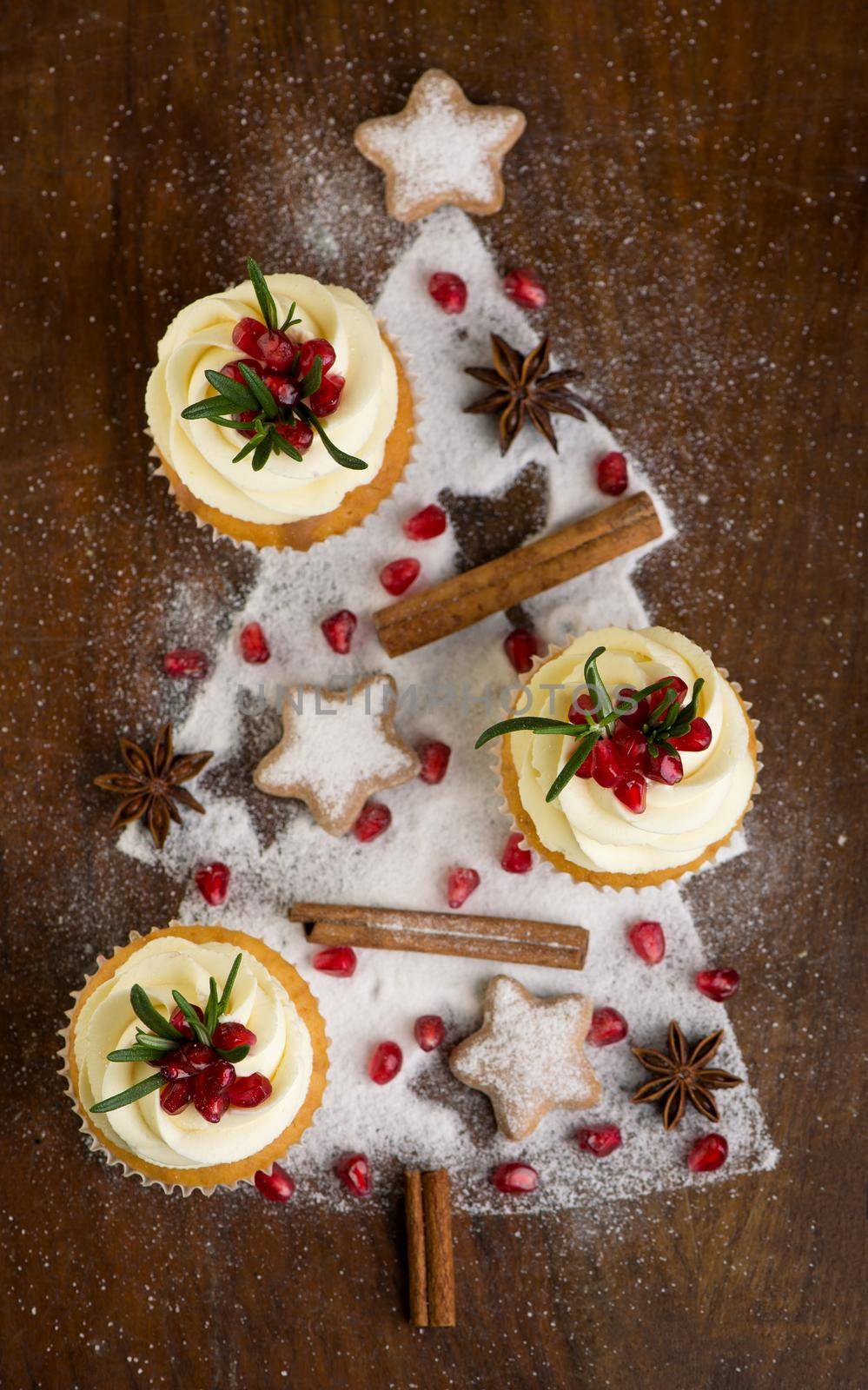 Christmas cupcakes with vanilla frosting, cranberries and rosemary on wooden background