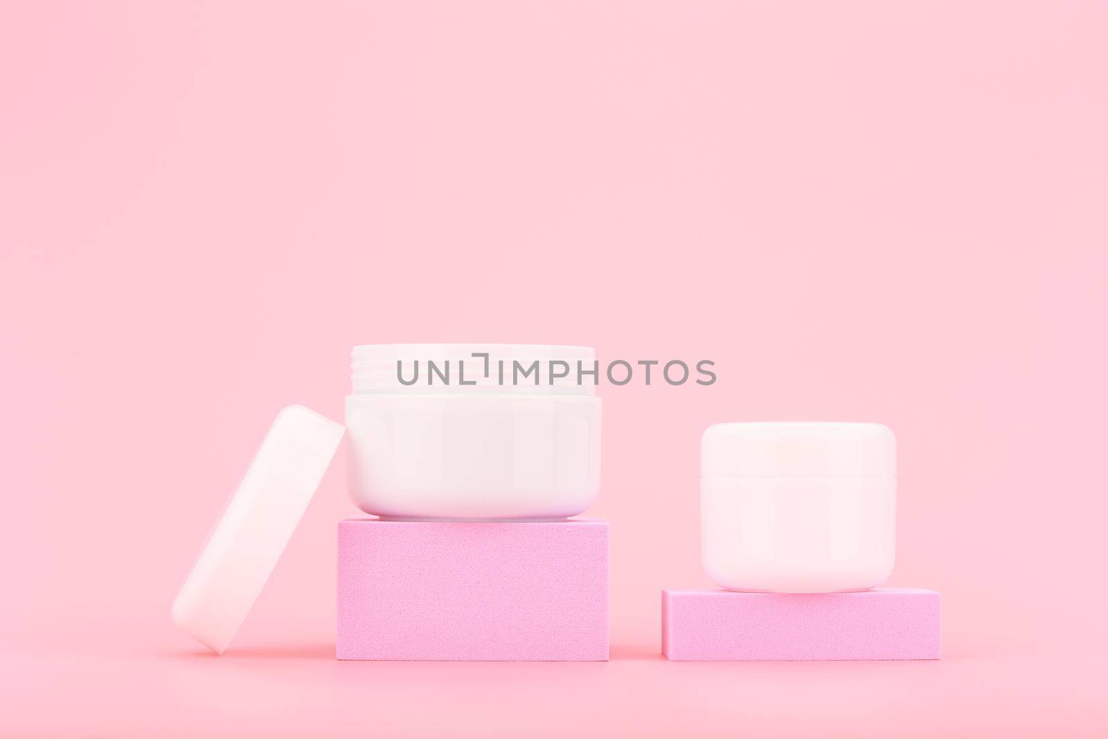 Two cosmetic cream containers on pink podiums against light pink background with copy space. Concept of beauty products for daily facial rituals or skin care routine