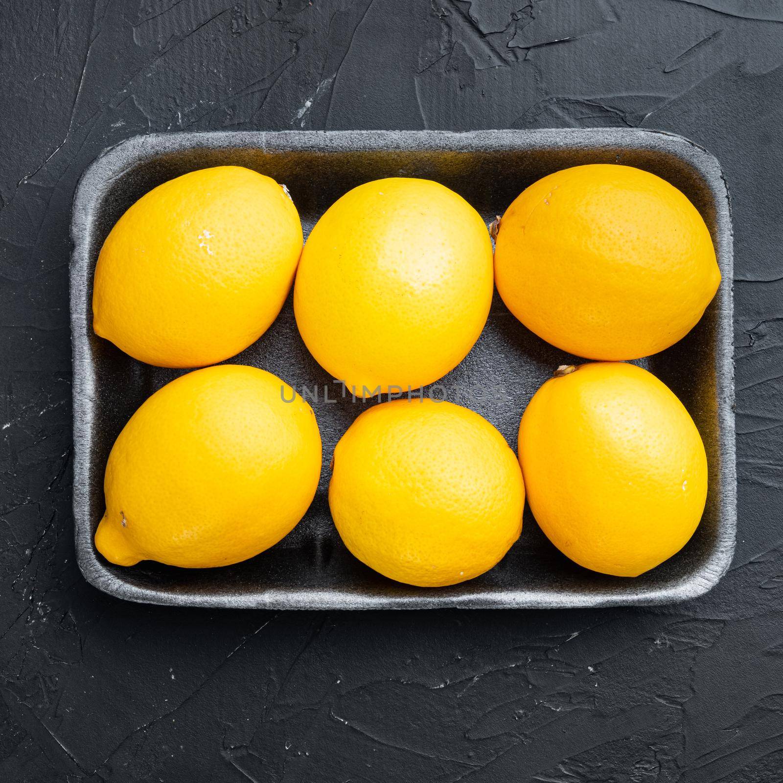 Ripe lemons set, in plastic tray, on black background, top view flat lay