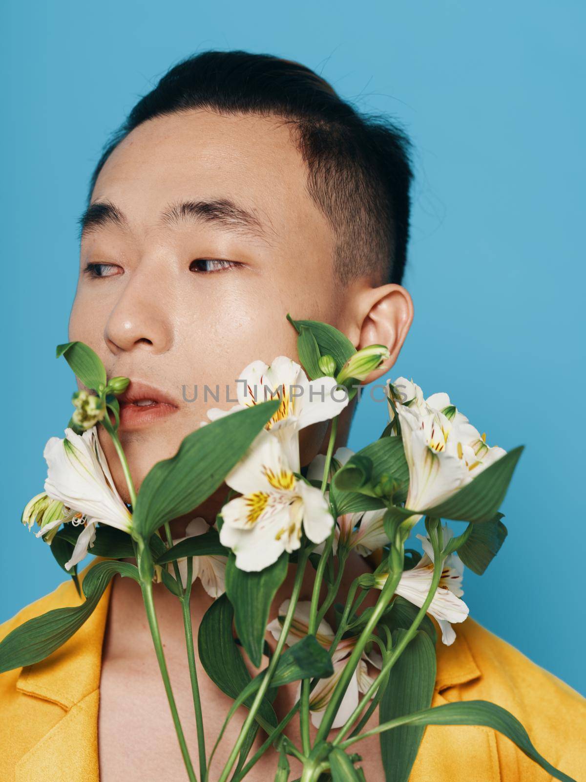 romantic asian guy with a bouquet of white flowers and in a yellow coat portrait close-up . High quality photo