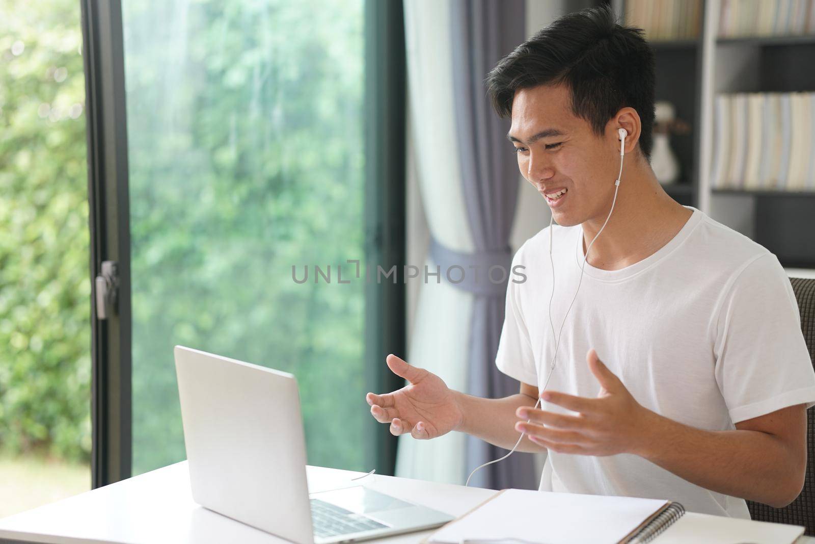 asian young teenage student man entrepreneur wear earphones working by video call conference studying learning online at home. e-learning webinar meeting. social distance in covid pandemic