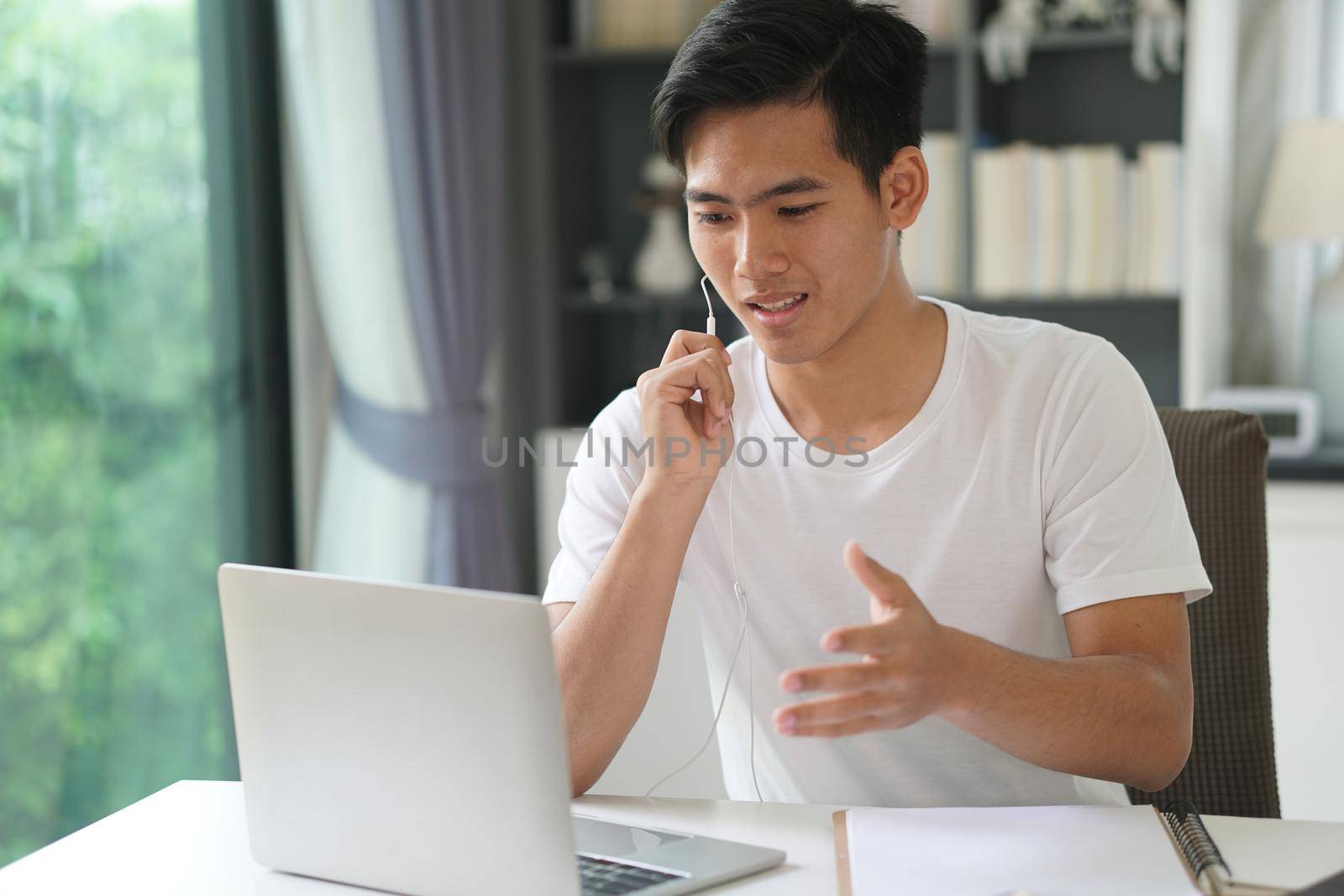 asian young teenage student man entrepreneur wear earphones working by video call conference studying learning online at home. e-learning webinar meeting. social distance in covid pandemic