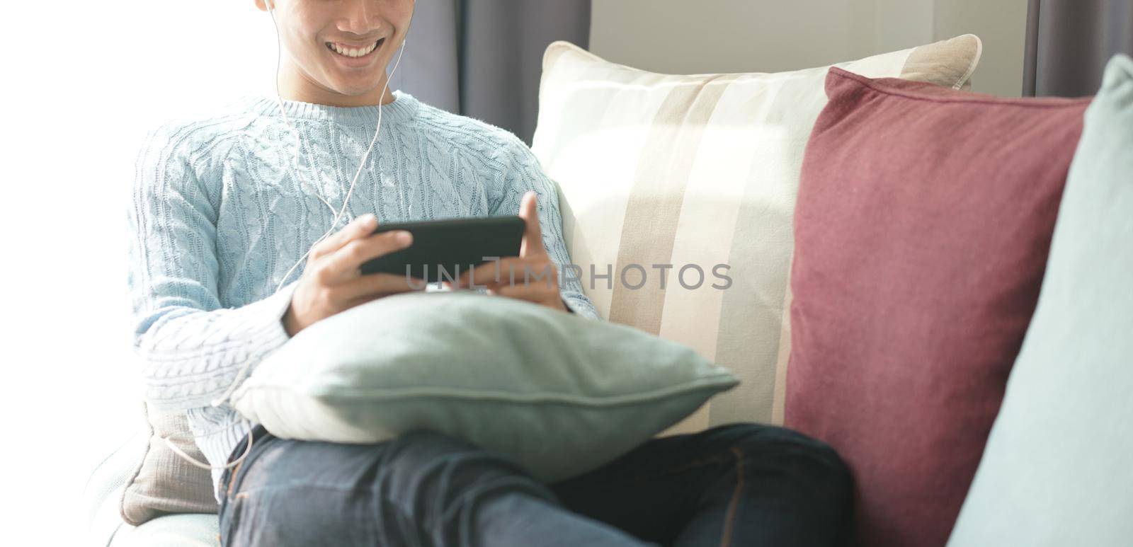 asian man wearing earphones listening to music on smart phone relaxing on sofa at home by pp99