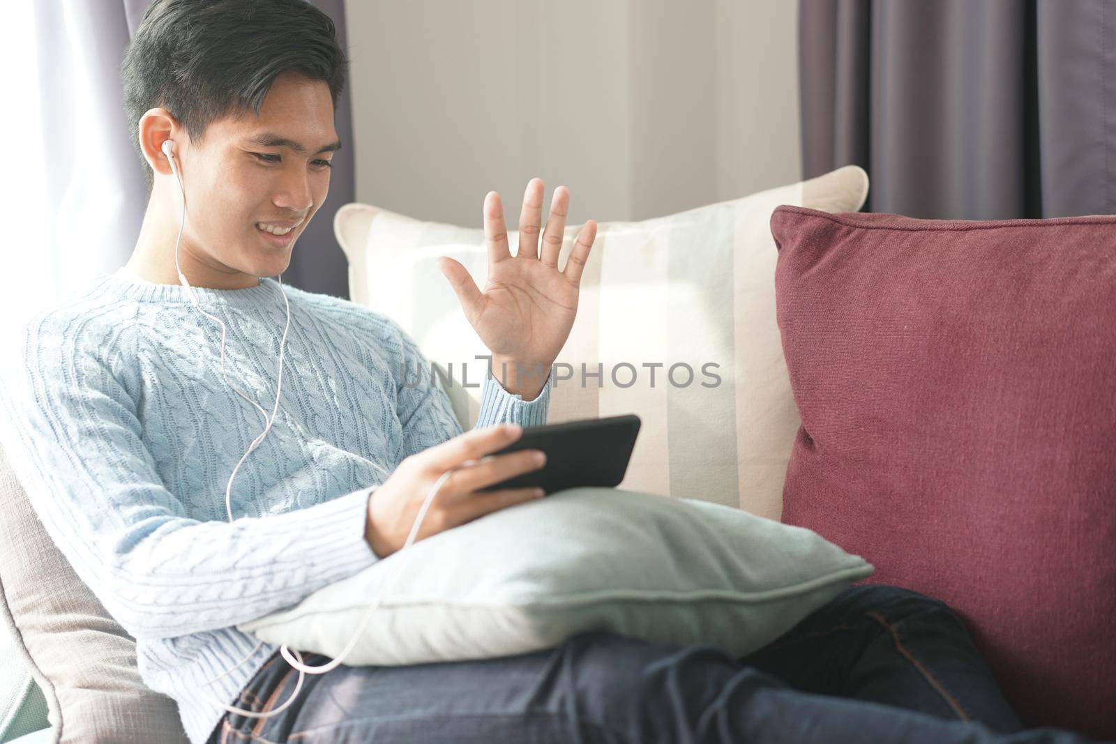 young asian man wearing earphones talking on video call meeting using smart mobile phone