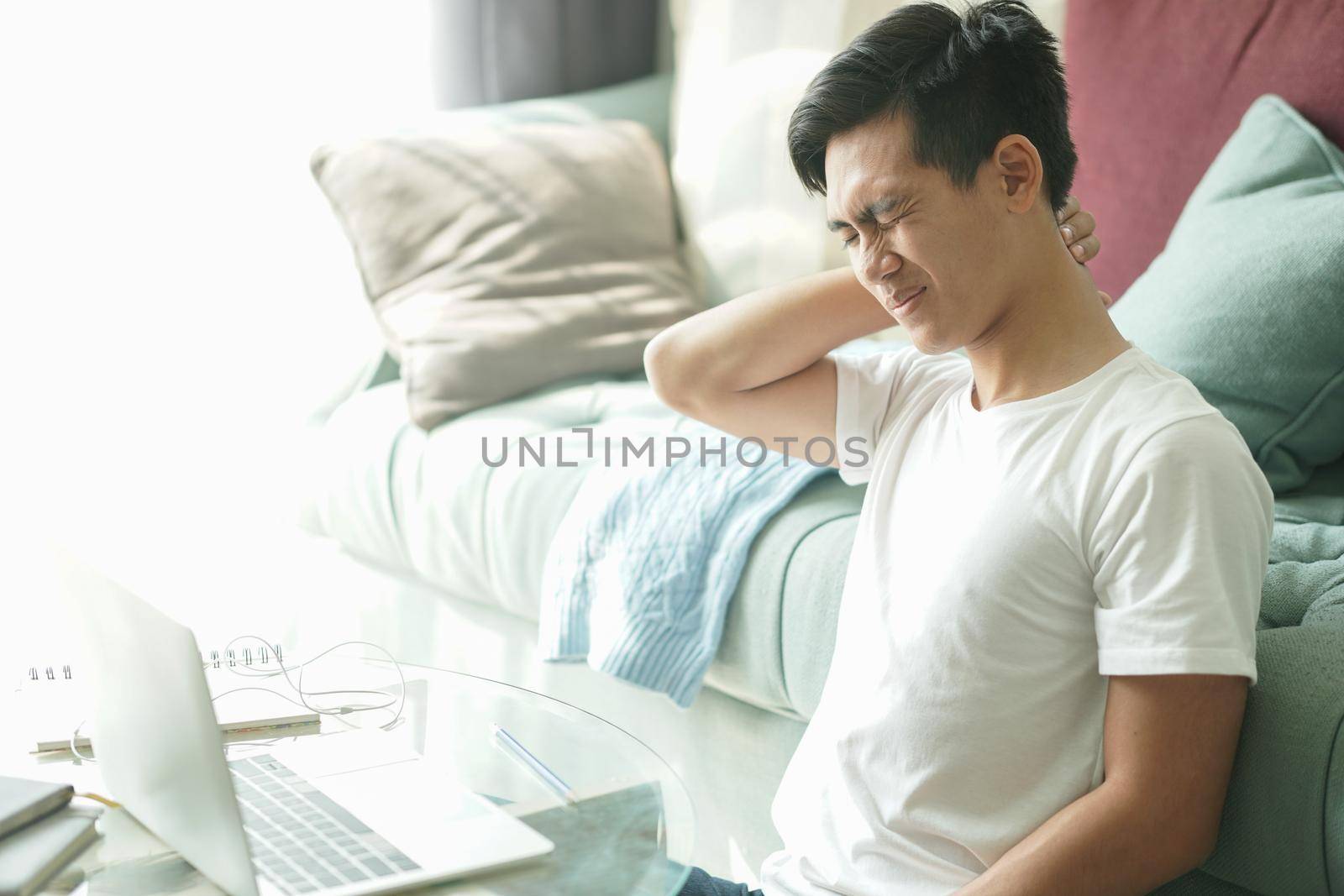tired exhausted frustrated asian young student man teenager entrepreneur suffering from neck pain while working at home