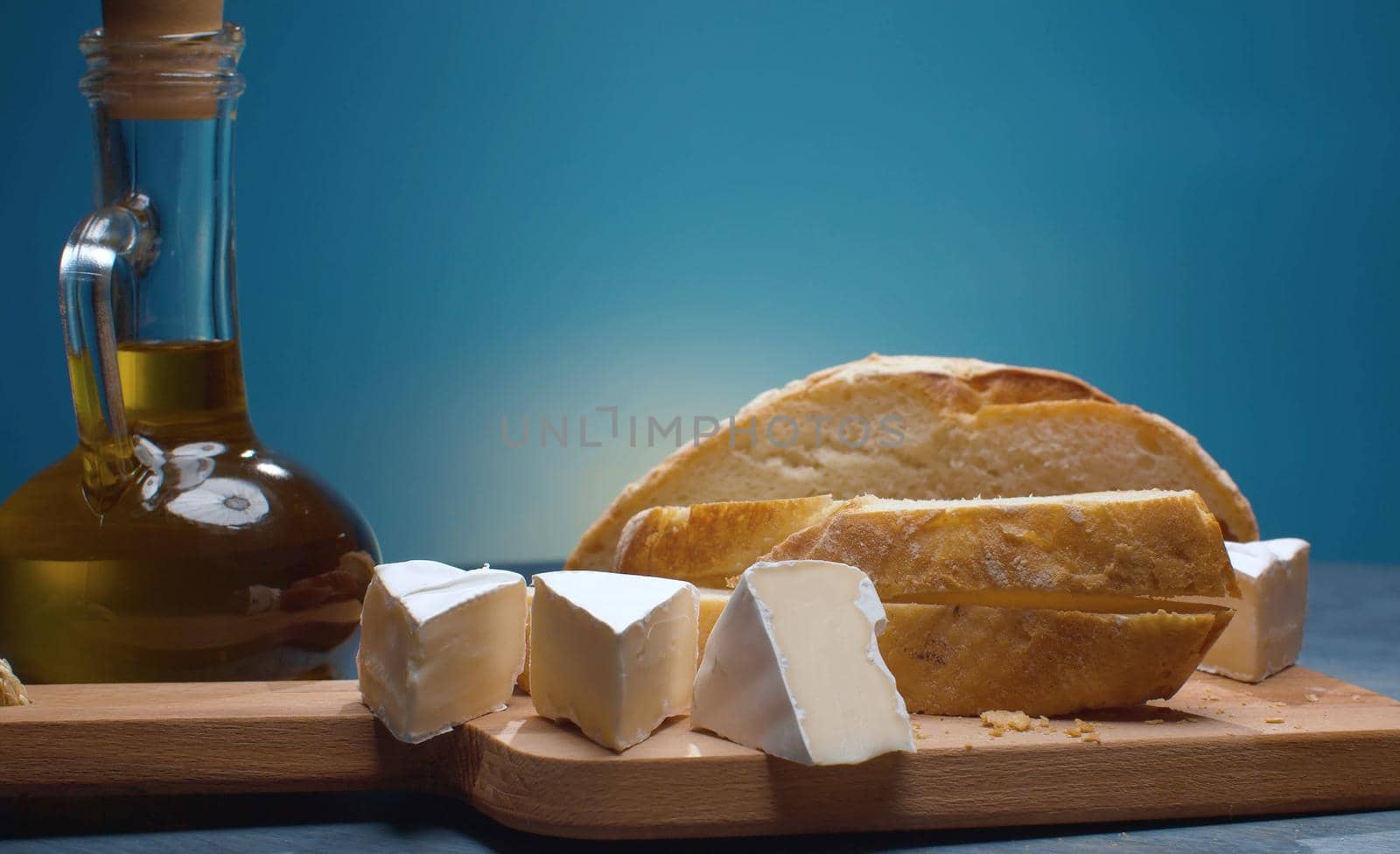 Close up olive oil, homemade bread and cheese on wooden cutting board. Blue background. Healthy fresh food concept