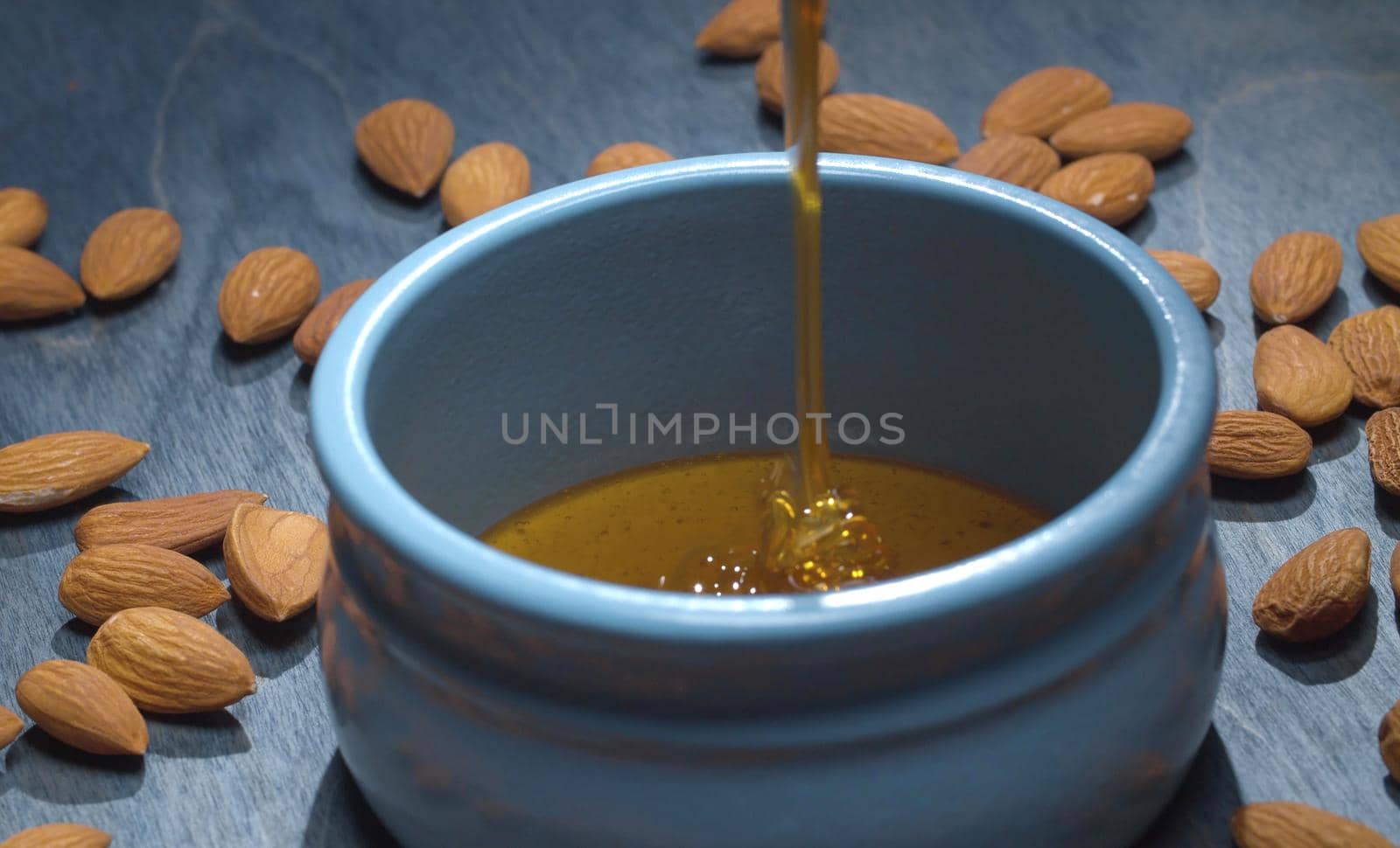 Close up fresh honey pouring into a bowl and almond nuts on blue background. Healthy fresh food concept