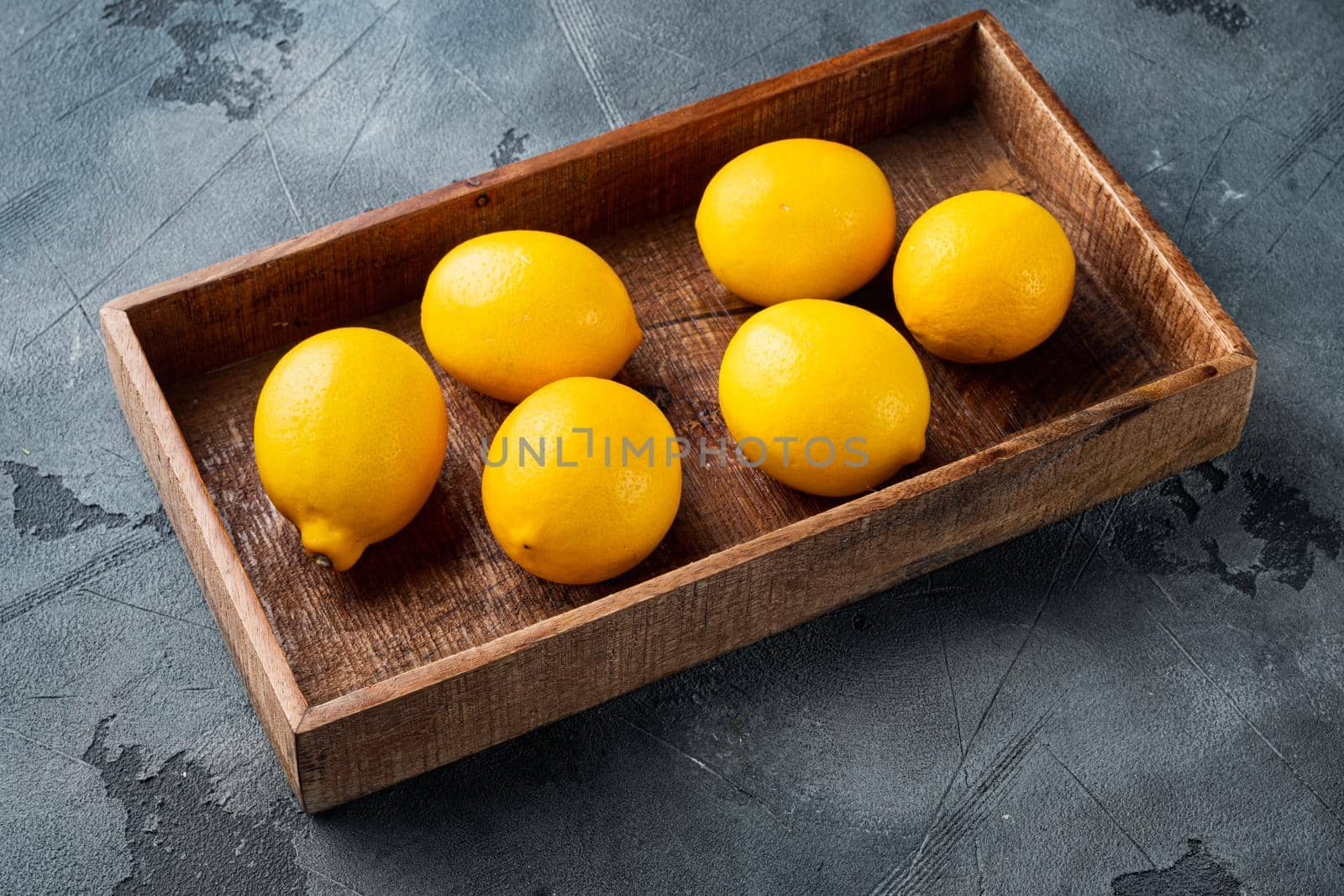 Fresh lemons set, in wooden box, on gray background