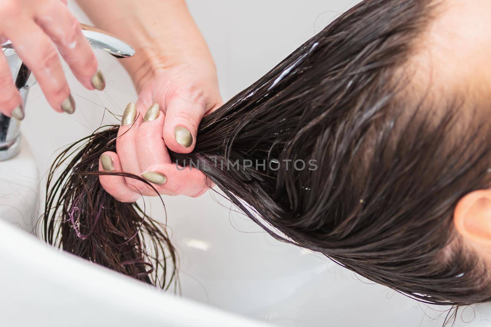 The hairdresser washes the head of a girl with long hair in the sink. Brown hair, close up