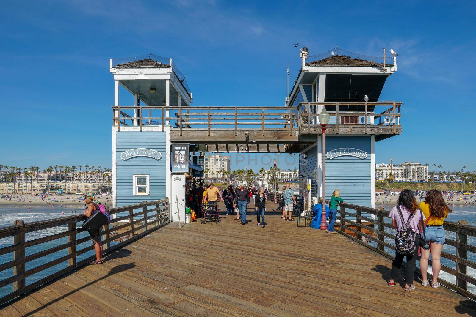 Tourist walking on the Oceanside Pier during blue summer day, Oceanside, northern San Diego County by Bonandbon