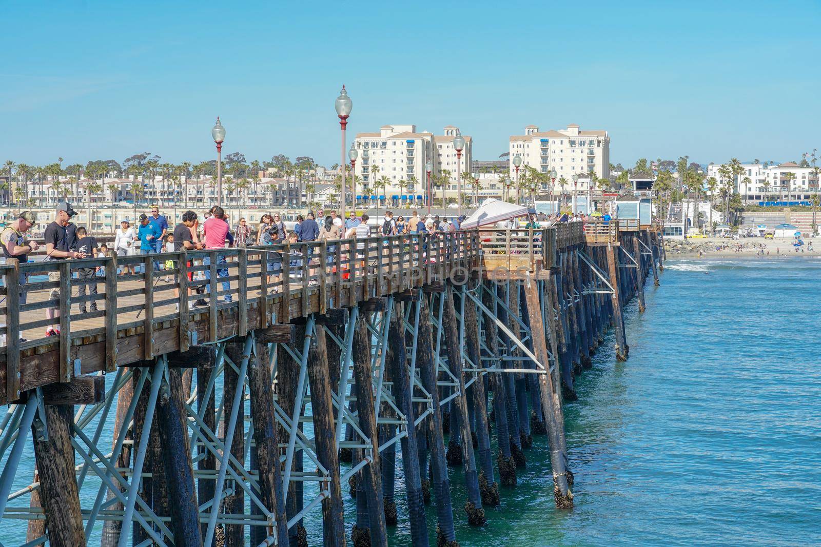 Tourist walking on the Oceanside Pier during blue summer day, Oceanside, northern San Diego County by Bonandbon