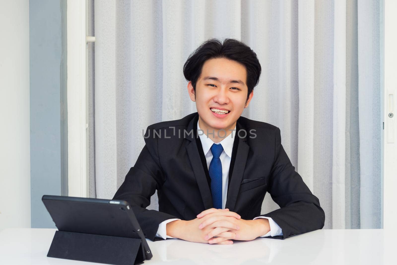 Work from home, Asian young businessman video conference call or facetime he smiling looking to camera sitting with hands on desk using smart digital tablet computer at home office