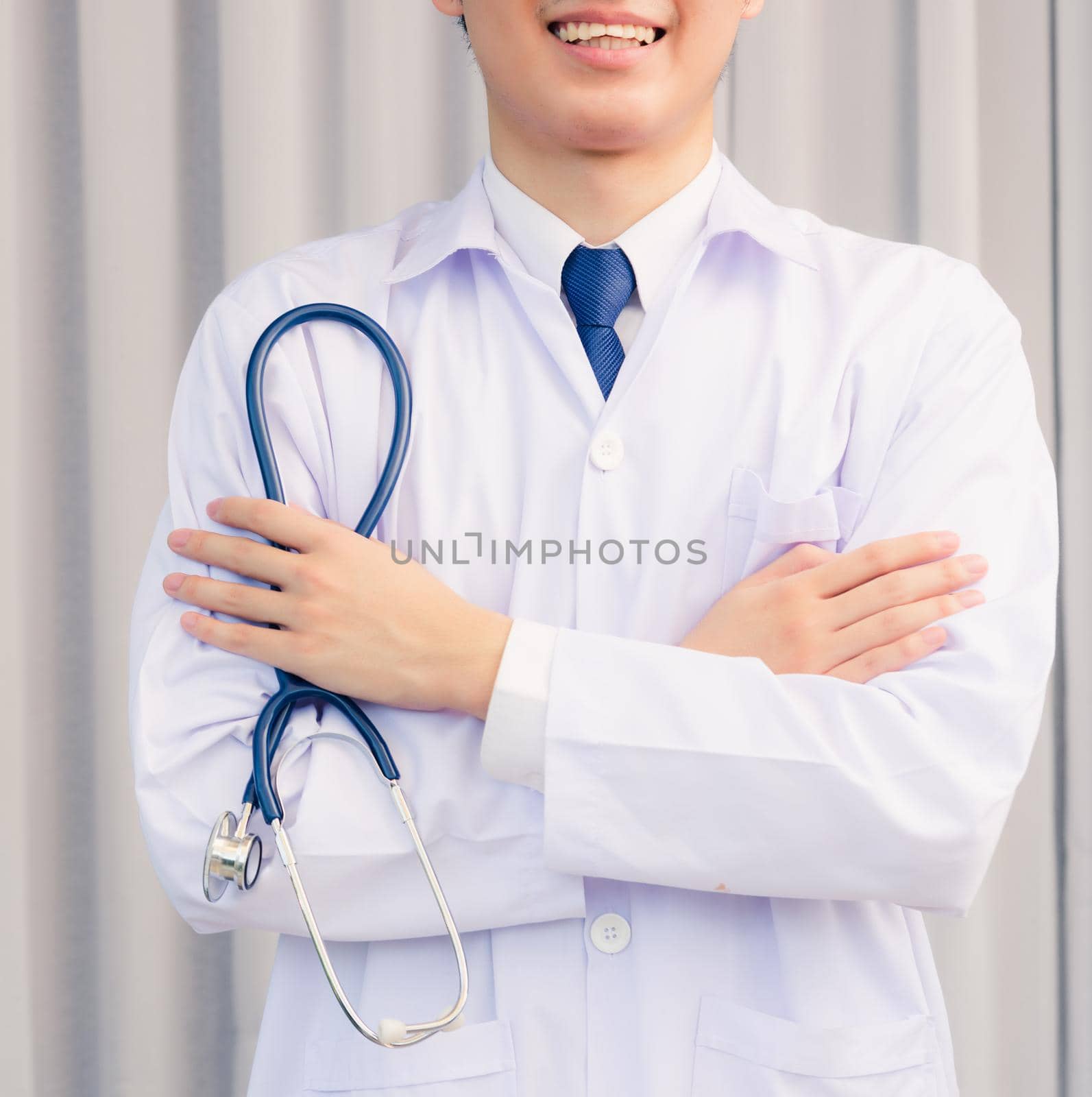 Portrait closeup of Happy Asian young doctor handsome man smiling in uniform stand crossed arm hold stethoscope on hand looking to camera with cop space, healthcare medicine concept