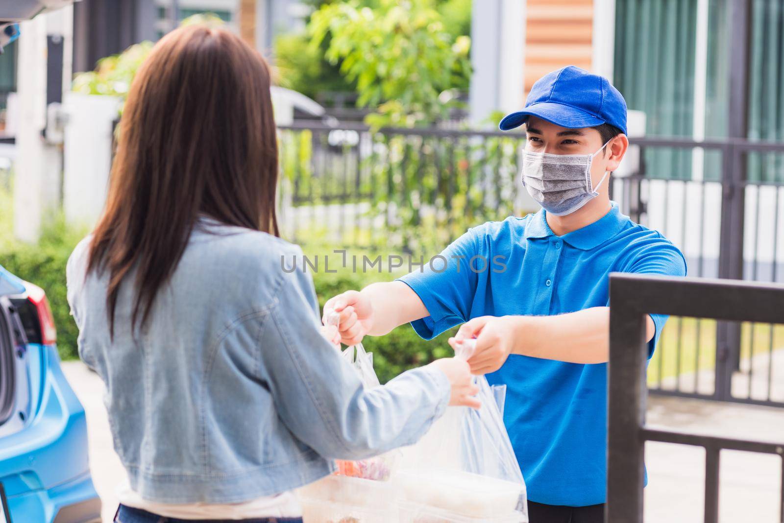 Asian young delivery man wear face mask he making grocery service giving rice food boxes plastic bags to woman customer receiving door at house after pandemic coronavirus, Back to new normal concept