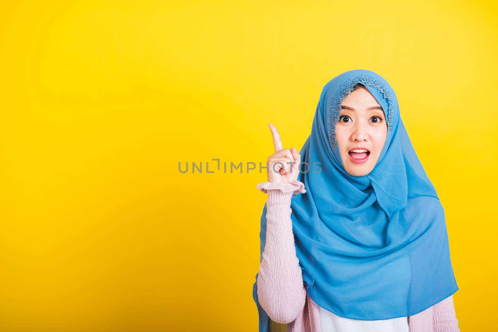 Asian Muslim Arab, Portrait of happy beautiful young woman Islam religious wear veil hijab funny smile she positive expression pointing with finger up to space isolated yellow background