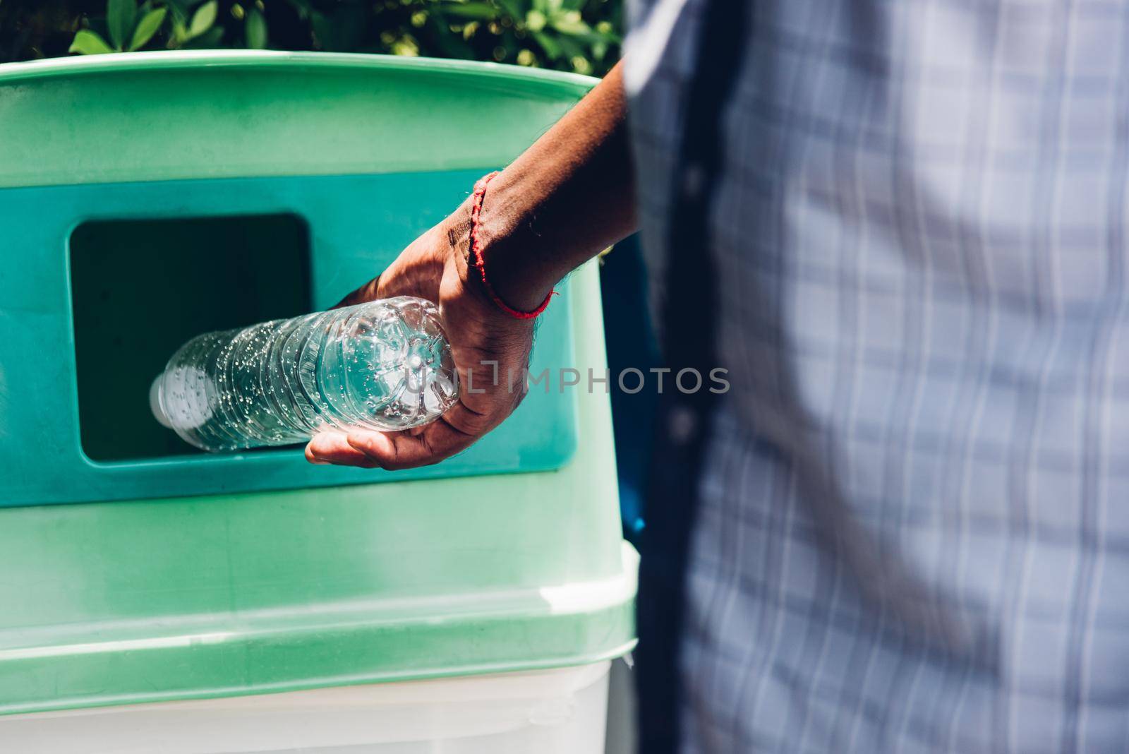 Selective focus close up the man black hand throwing an empty plastic water bottle in the recycling garbage trash or bin, environmental recycling concept 