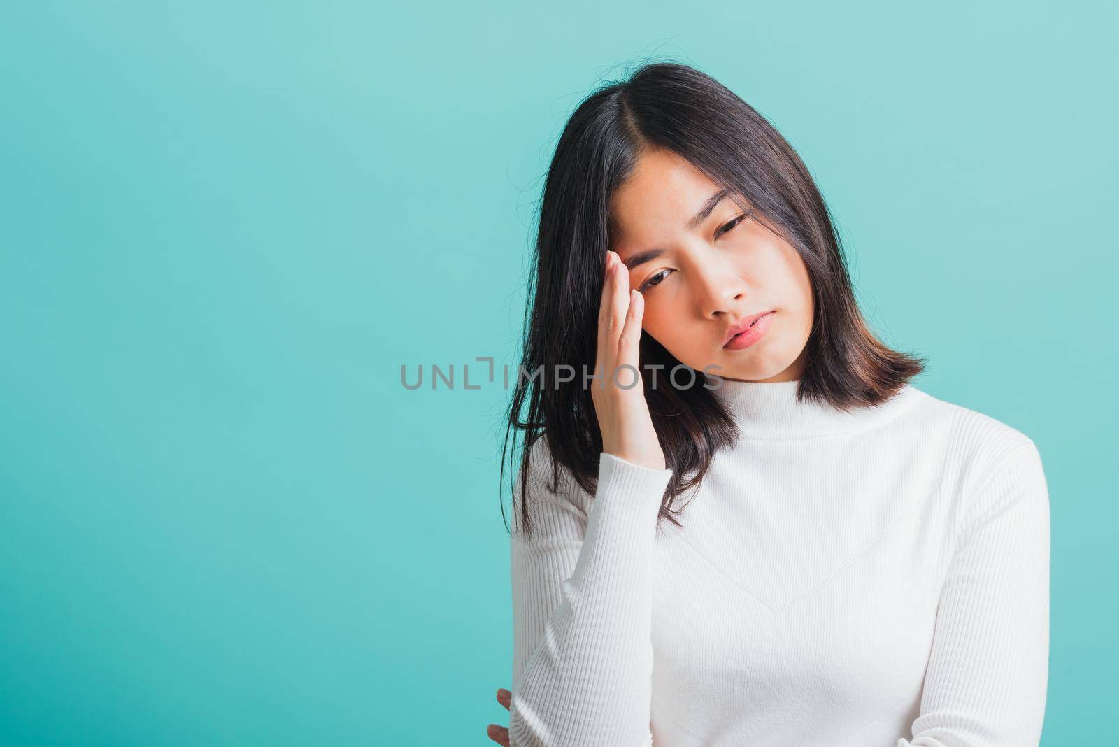 Young beautiful Asian woman holding her hands to her temples with a severe headache, Portrait sad female unhappy suffering from migraine, studio shot isolated on a blue background