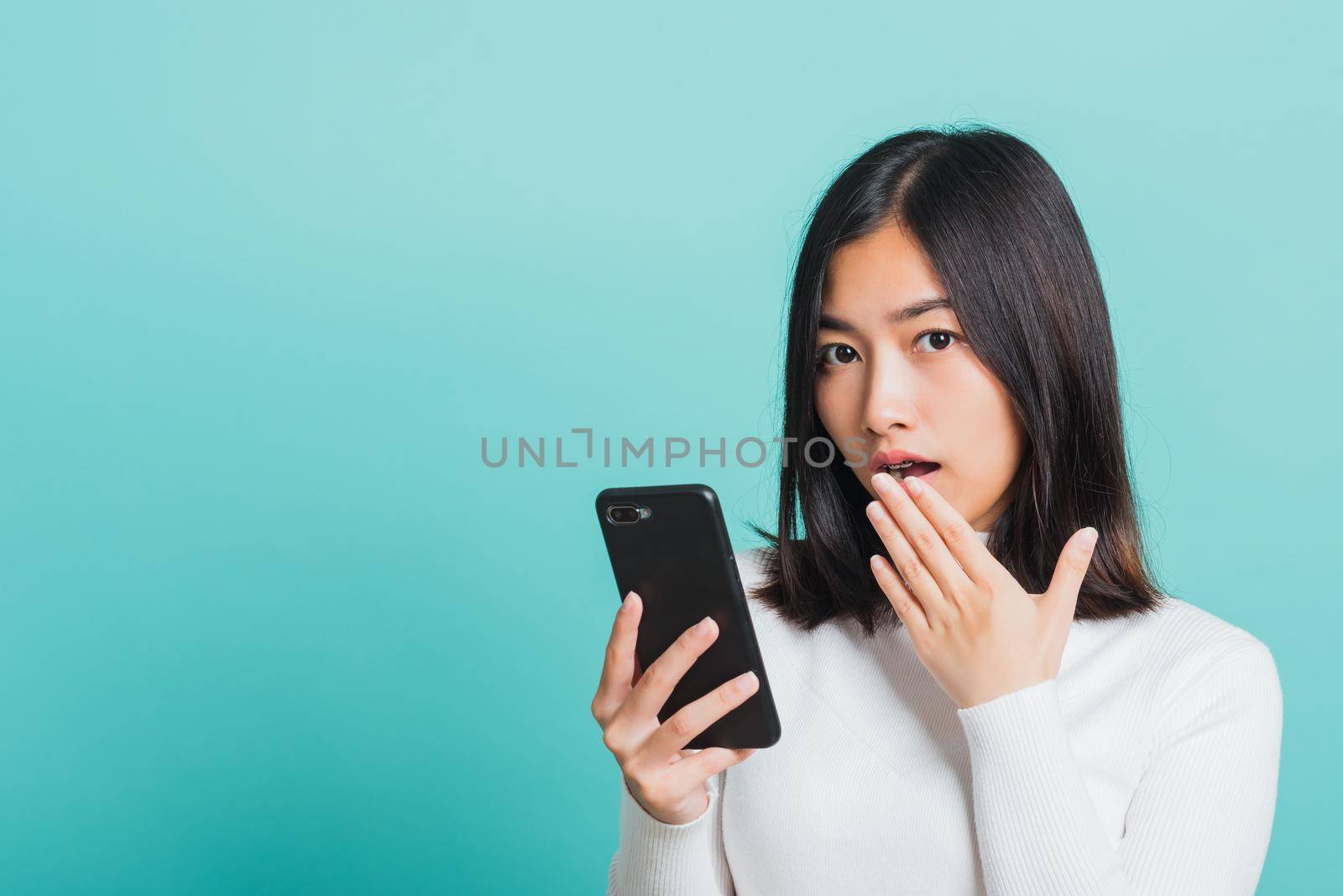 Portrait female anxious scared on the phone seeing bad news, Young beautiful Asian woman surprised shocked with mobile phone close mouth with palm, studio shot isolated on a blue background